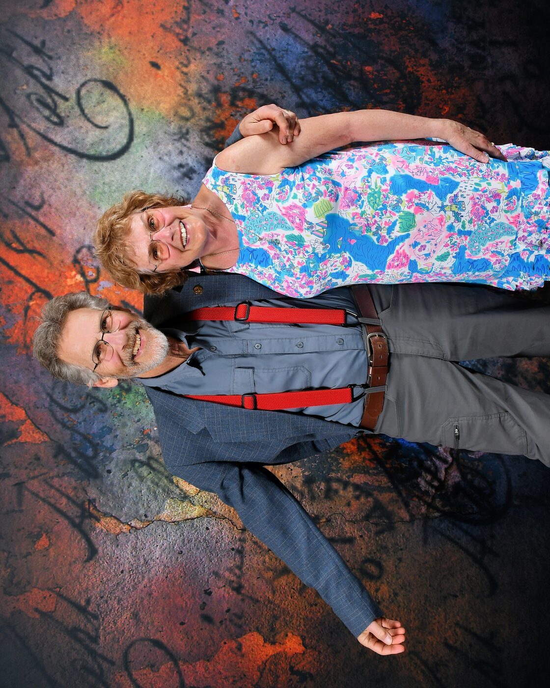 Woman in a floral dress and a man in red suspenders, painted backdrop