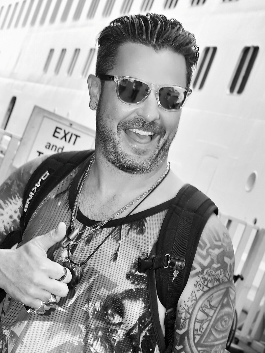 Black and white candid of a man in sunglasses giving a thumbs up beside the ship