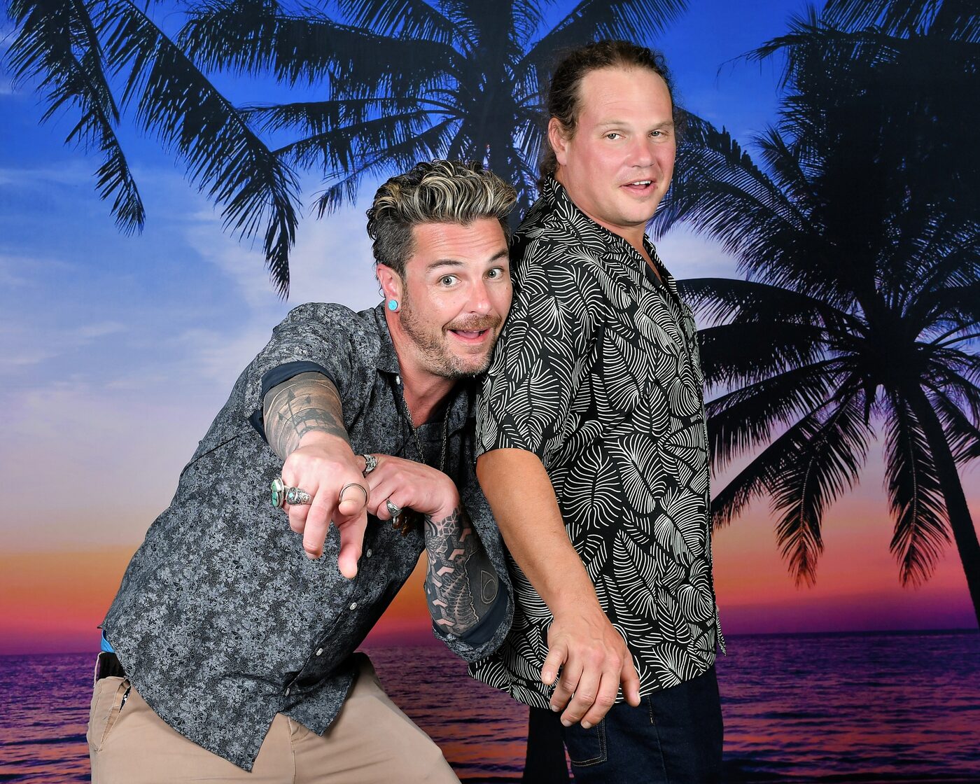Two men clowning in front of a sunset palm backdrop
